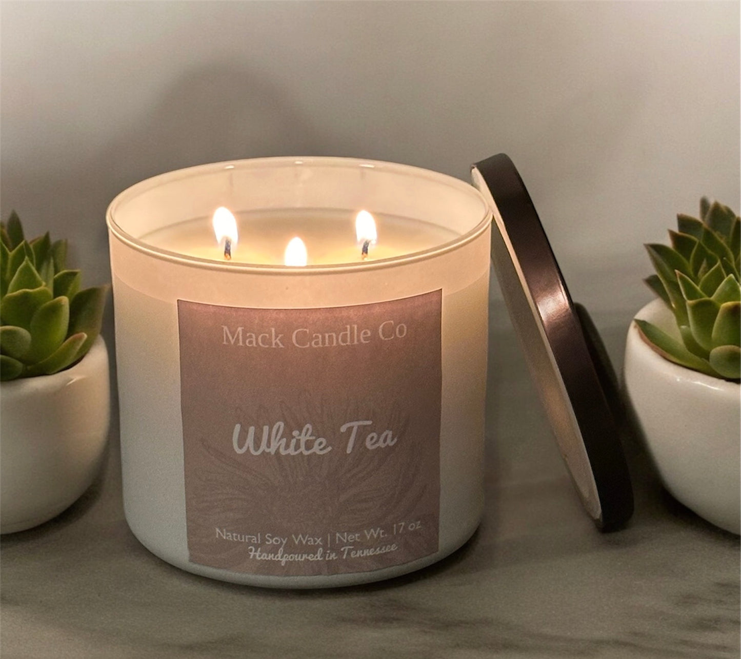 Luxury triple wick White Tea Soy Candle, comes in a matte white jar filling the space of a living room. Non toxic clean burning handpoured in small batches in Nashville Tennessee. 